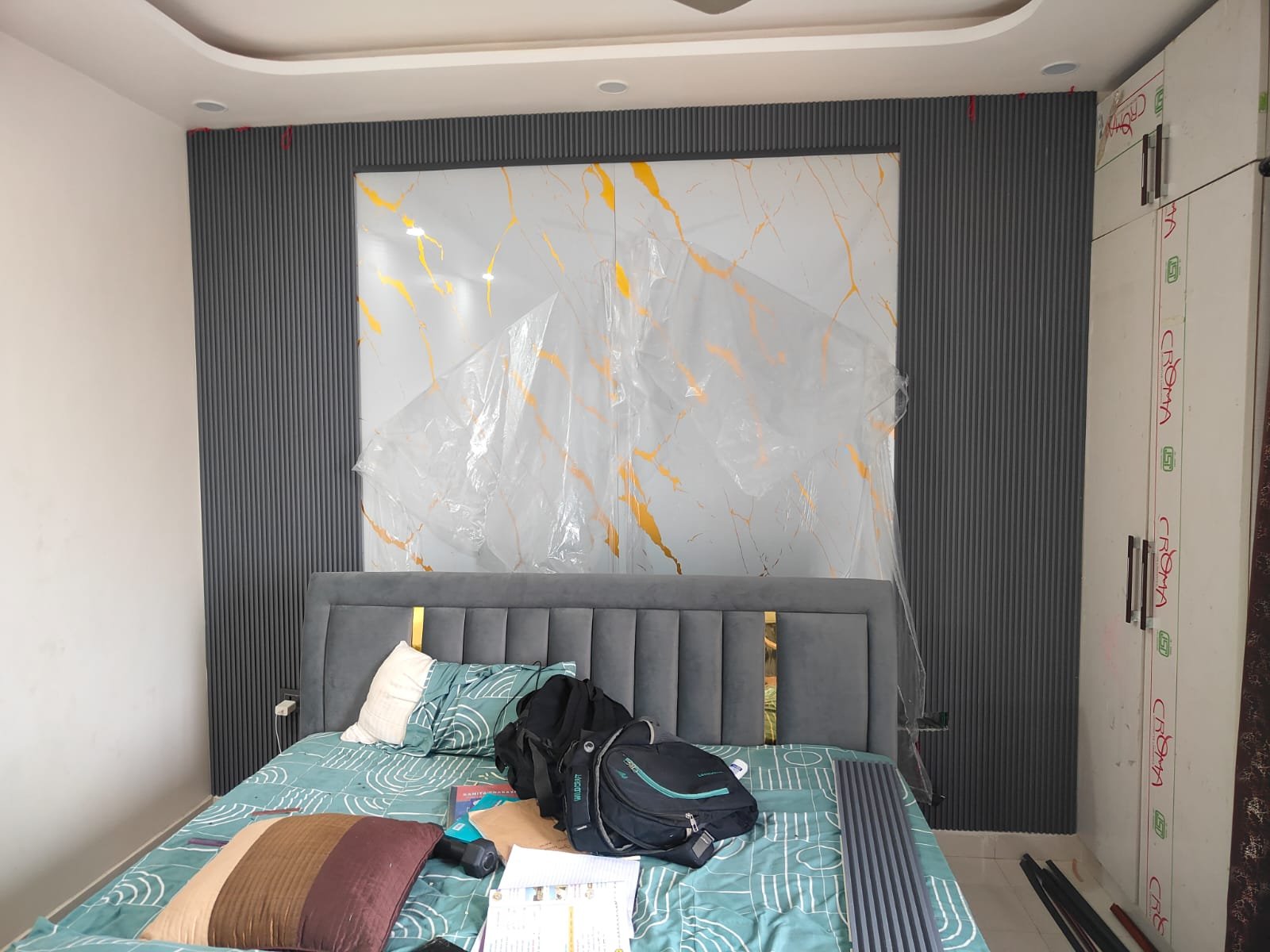 Bedroom feature wall with wallpaper, wooden fluted panels and warm lighting behind the bed